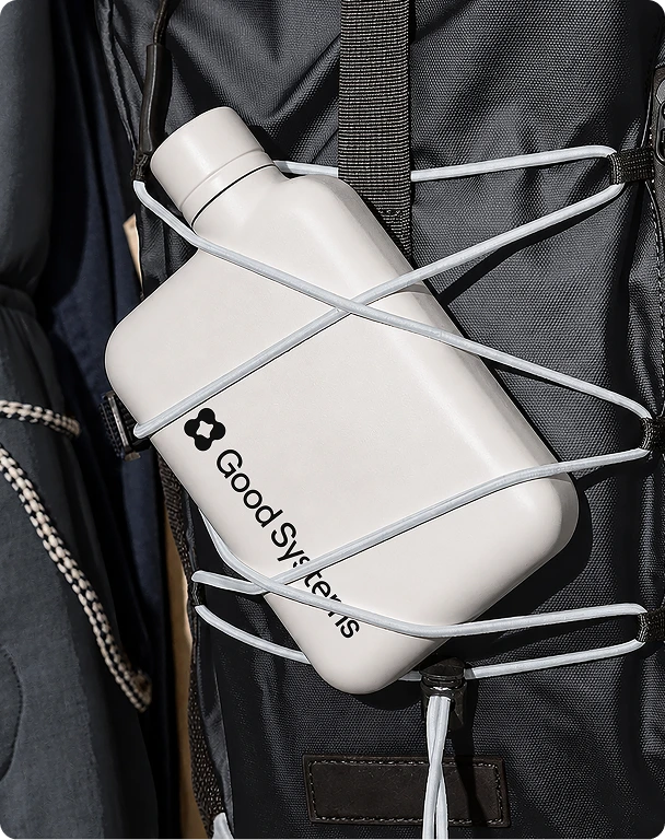 White flask with the Good Systems lockup, strapped to a backpack