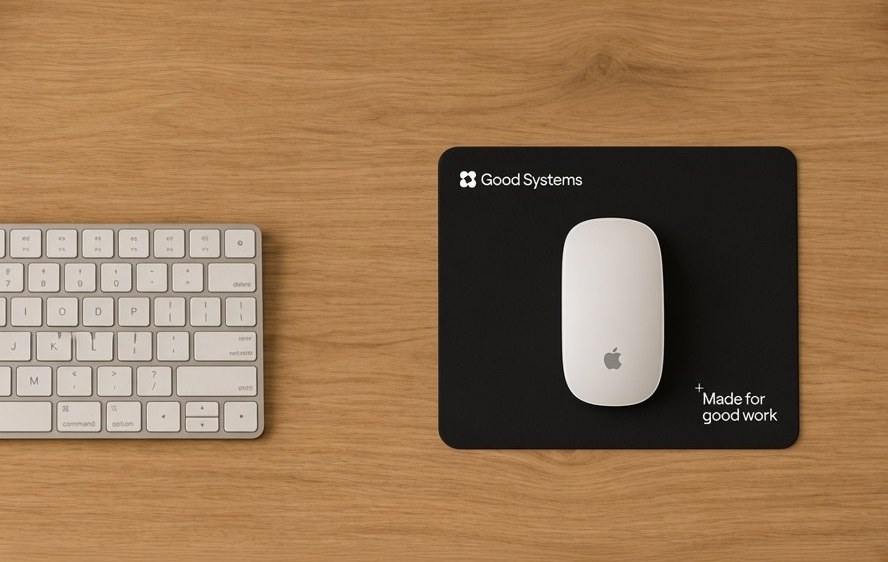Black mouse pad with lockup and endline on a desk, beside keyboard and monitor