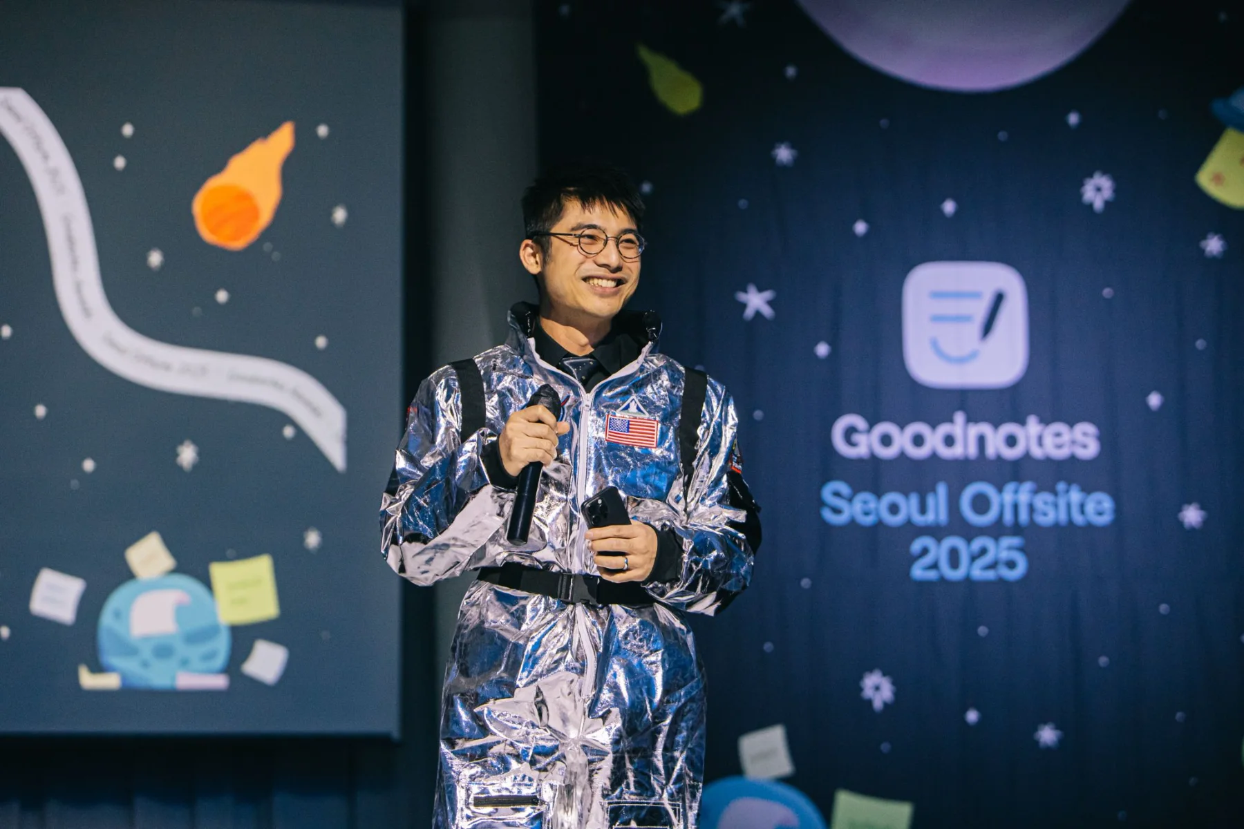A presenter in a space suit in front of the illustrated stage screens
